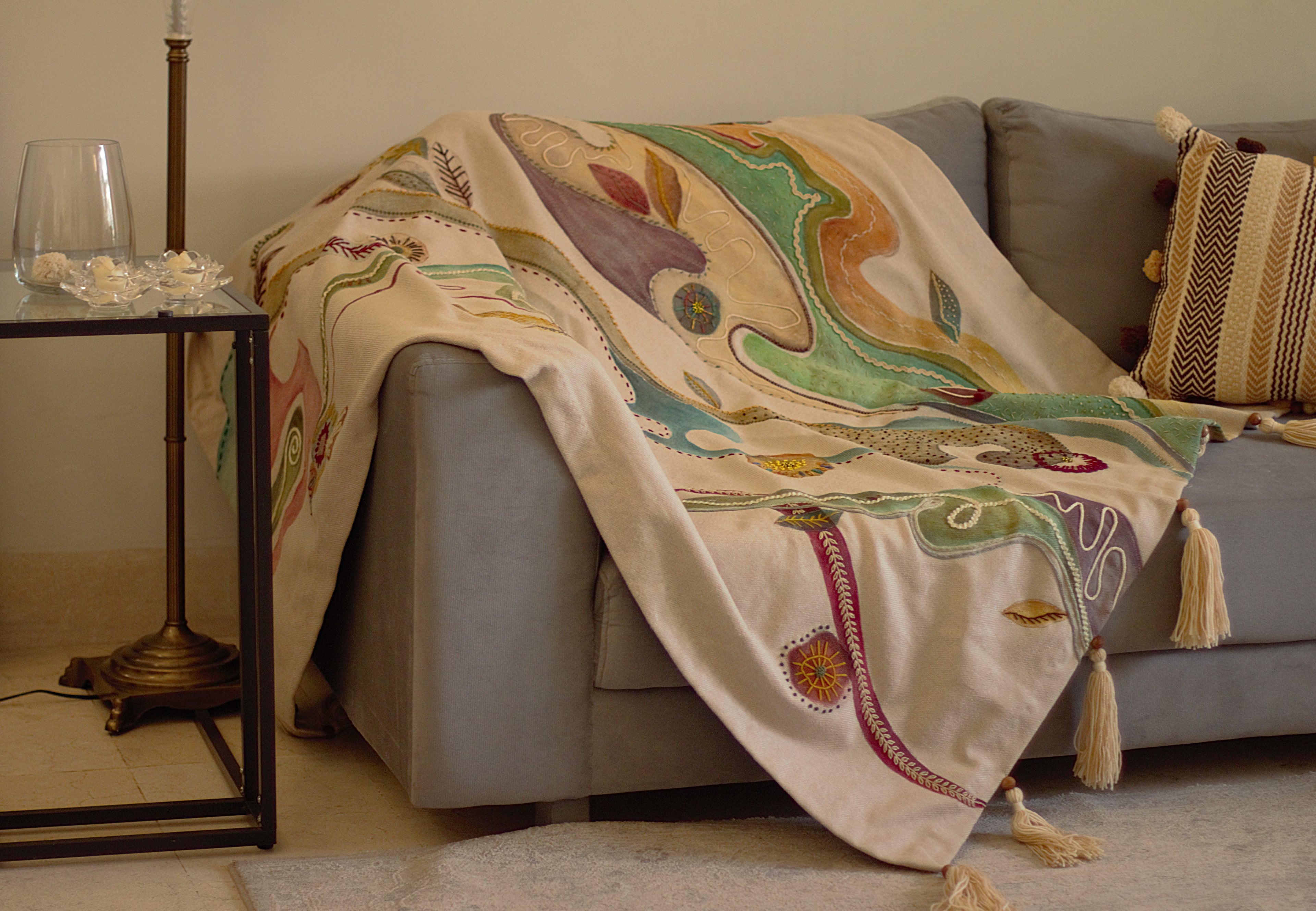 Decorative blanket / throw with abstract patterns draped over a sofa in a living room. Hand painted