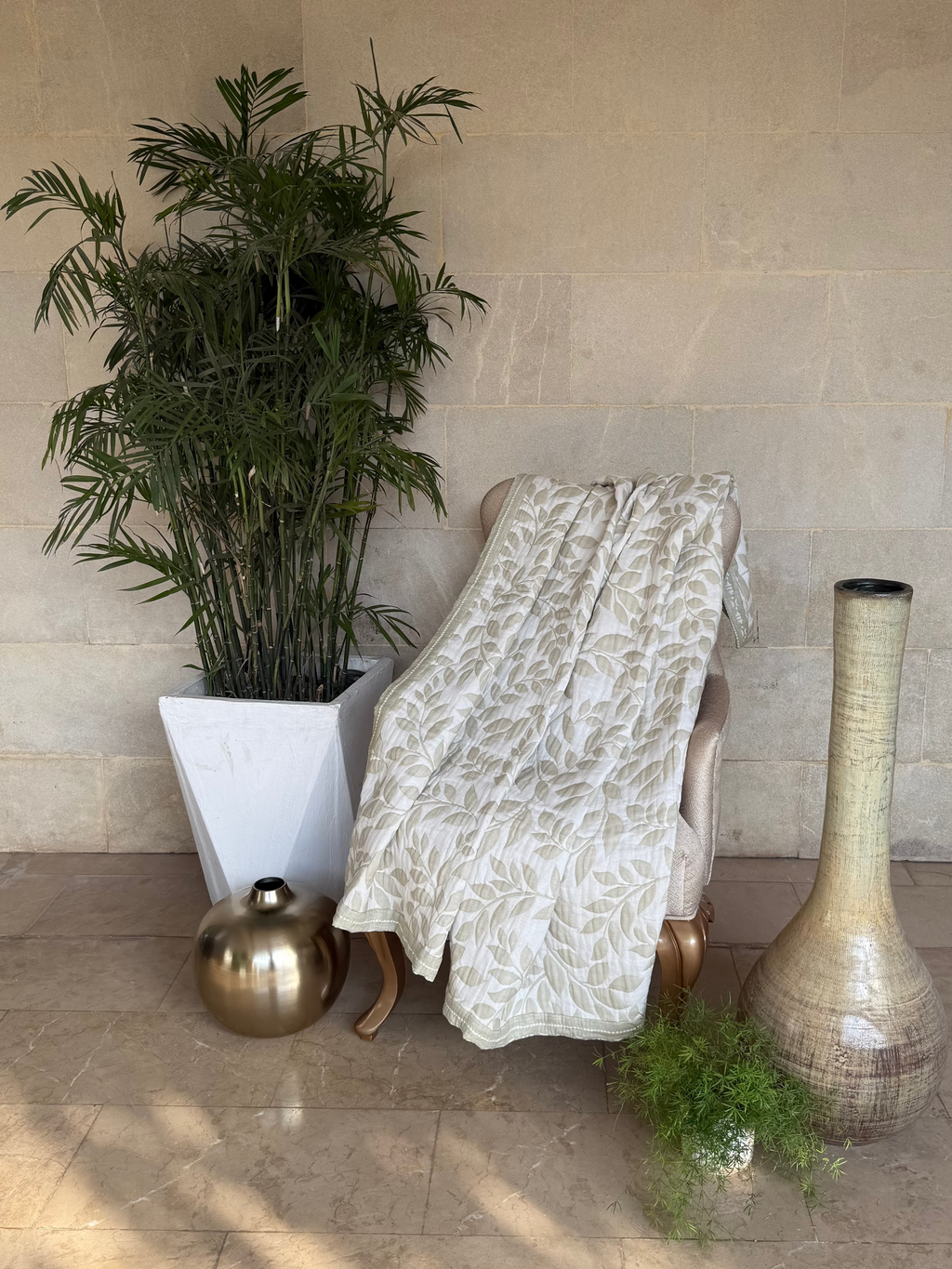 A green & off-white upholstered lounge chair draped with a patterned throw blanket.