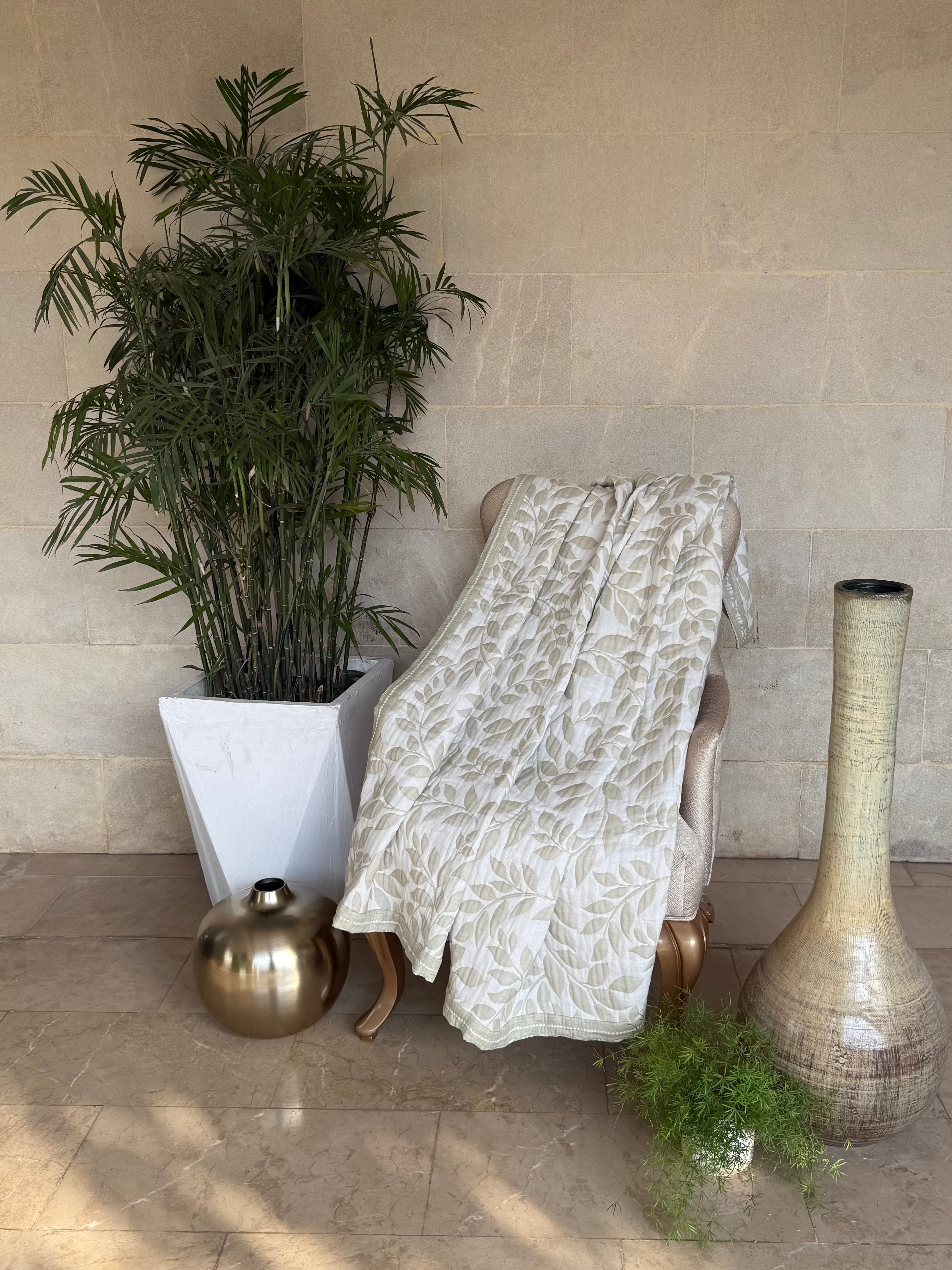 A green & off-white upholstered lounge chair draped with a patterned throw blanket.